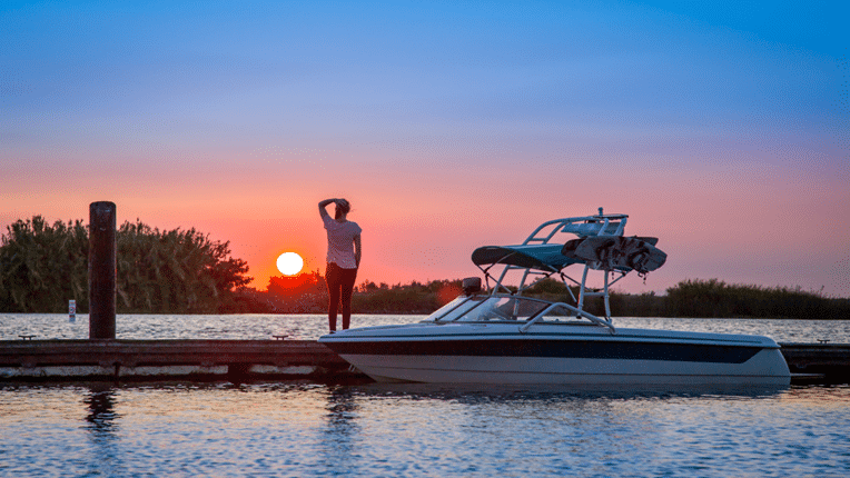 Girl standing on pier next to wakeboard boat at sunset